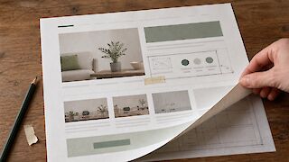A printed website with a careful paper repair and one corner lifted to reveal its underlying layout structure.